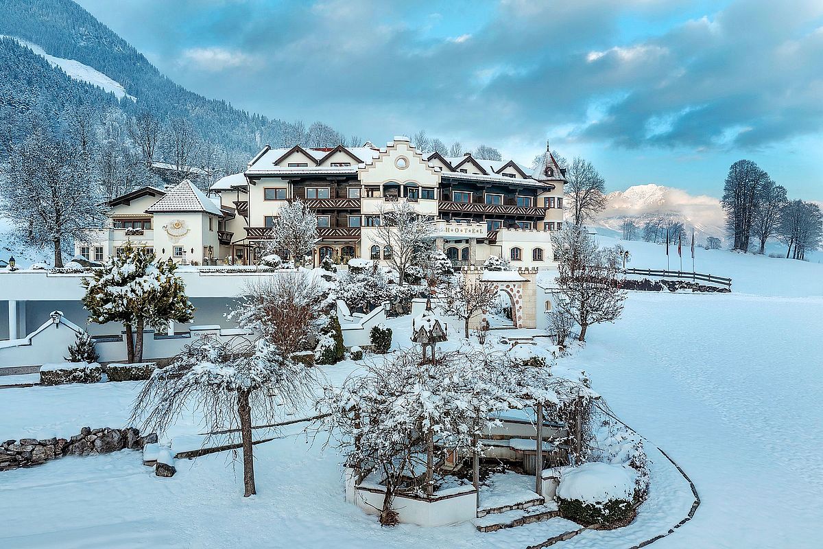 Hotel AlpenSchlössl in der Ferienregion Söll im Winter Winteransicht des 4-Sterne-Hotels AlpenSchlössl in Söll, umgeben von verschneiten Wiesen und der Bergwelt am Wilden Kaiser.